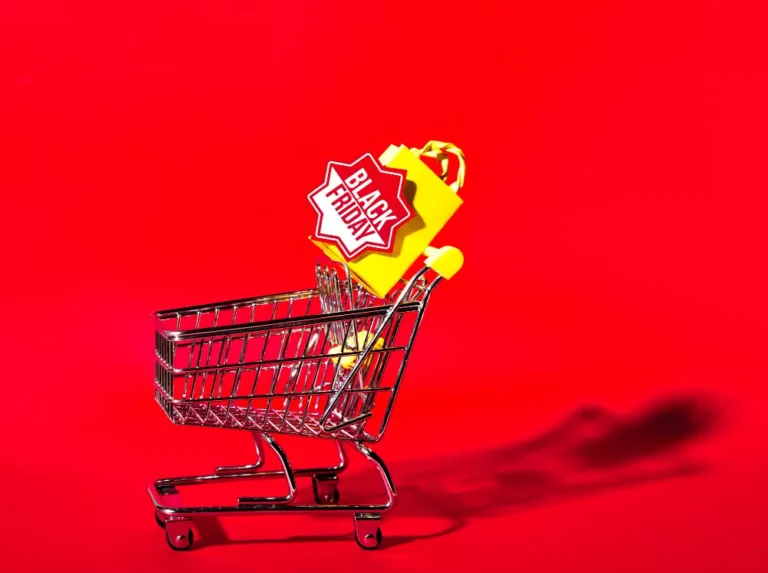 Shopping cart with yellow bag and Black Friday tag on red background, promoting sales and discounts for online shopping deals.