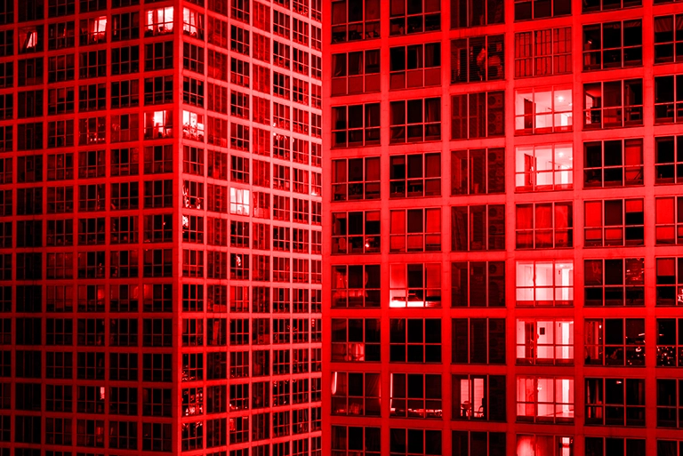 Red-tinted high-rise buildings with illuminated windows, modern urban architecture symbolizing the real estate industry.
